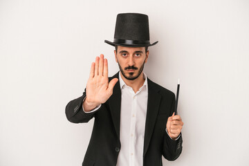 Young magician man holding wand isolated on white background standing with outstretched hand showing stop sign, preventing you.