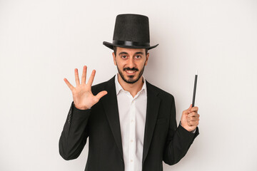 Young magician man holding wand isolated on white background smiling cheerful showing number five with fingers.