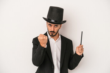 Young magician man holding wand isolated on white background showing fist to camera, aggressive facial expression.