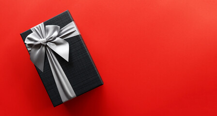 Black gift box on red background with copy space.