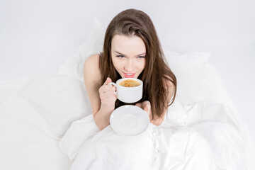 A woman sits in bed and takes a sip of aromatic coffee. Tasty breakfast. The brunette is holding a...