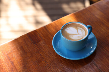 Ceramic cup of aromatic coffee with foam on wooden table in outdoor cafe. Space for text