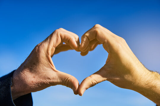 Love Has No Age Concet. Lgbt Gay Couple With Different Ages Form Heart Shape With Hands Over Blue Sky At Sunny Morning