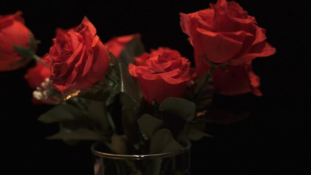 A glass jar with plastic red roses flowers over black background