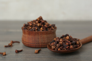 Spoon and bowl of aromatic dry cloves on wooden table