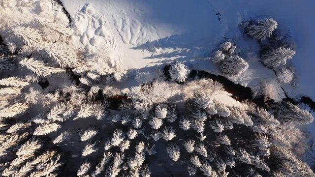 Survol drone vertical d&rsquo;une rivi&egrave;re qui serpente dans une for&ecirc;t enneig&eacute;e. Paysage d&rsquo;hiver, neige, Jura.