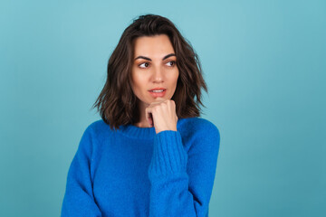 A woman in a blue knitted sweater and natural make-up, curly short hair, looks away thoughtfully, thinking about ideas