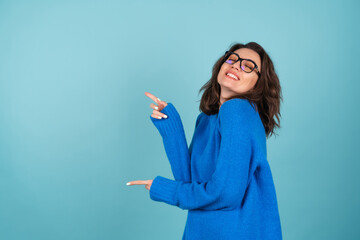 A woman in a blue knitted sweater, curly short hair, glasses on her eyes, smiles cheerfully,...