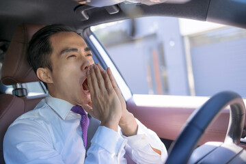 Young businessman looks tired yawning while driving the car