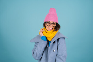 Spring autumn portrait of a woman in a blue knitted sweater, glasses, a yellow bright scarf and a gray coat, smiling cheerfully, posing fashionably, in pink hat