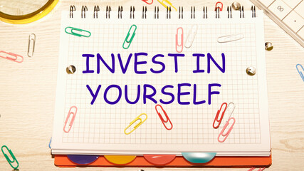 invest in yourself text on a notebook in a cage with scattered paper clips on a notebook and a table