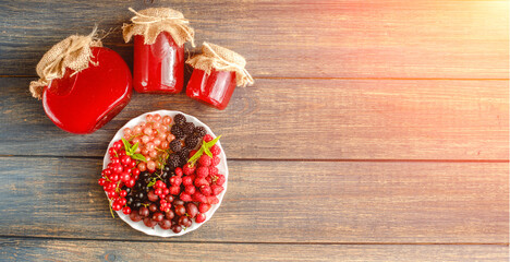 Assorted fresh summer berries and jam in jars. Raspberries, gooseberries, blackberries, currants, wild strawberries, strawberries.