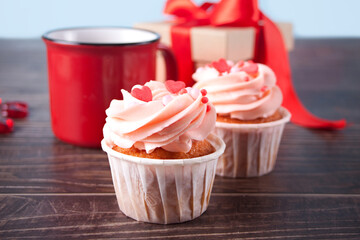 Valentines cupcakes cream cheese frosting decorated with heart candy, mug of coffee and gift box on the wooden background.