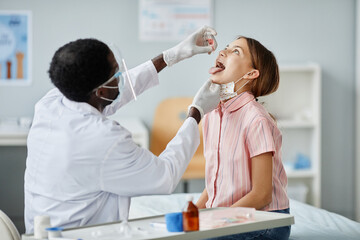 Portrait of African-American of doctor dropping liquid in mouth of child during oral vaccination in clinic