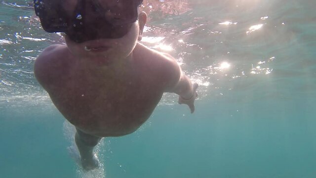 A child in an underwater mask learns to swim and dive. The boy dives into the sea.
