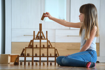 Creative child girl playing with game stacking wooden toy blocks in high building structure. Hand...