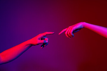 Two human hands trying to touch each other isolated on purple background in neon light. Concept of human relation, community, togetherness, symbolism, culture and history - obrazy, fototapety, plakaty