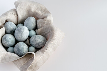Marble-colored Easter eggs in a basket with a linen napkin on a white background. Easter greeting card with place for text.
