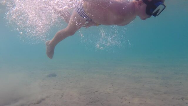 A child in an underwater mask learns to swim and dive. The boy dives into the sea.
