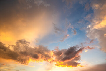 Dramatic sunset sky landscape with puffy clouds lit by orange setting sun and blue heavens