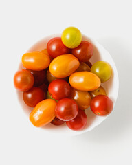 Various cherry tomatoes in bowl on white background.