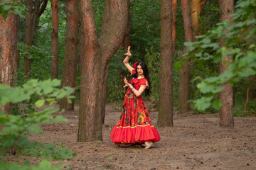 Gypsy woman. Red long dress. Portrait of a girl in an ethnic costume in the forest. The gypsy brunette is beautiful. - obrazy, fototapety, plakaty