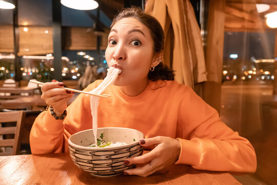 Asian woman eating Vietnamese noodle soup using chopsticks in restaurant