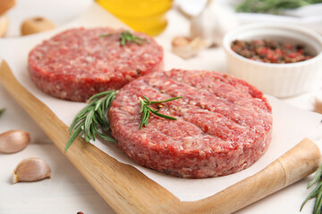 Raw hamburger patties with rosemary on white wooden table, closeup
