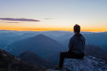 Naklejka na ściany i meble Hiker sitting on top of the hill waiting for sunrise and enjoying scenic view