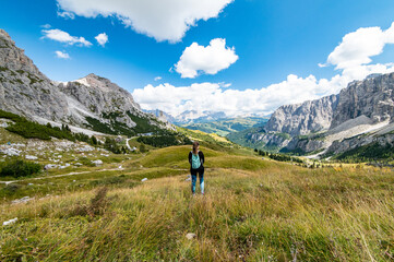 Aerial view of female hiker looking at Gardena Pass, Sass da Ciampac, Tor Bornech and Sass dla Luesa, Trentino Alto Adige, Italy. Alpine meadows and Passo Gardena. - obrazy, fototapety, plakaty