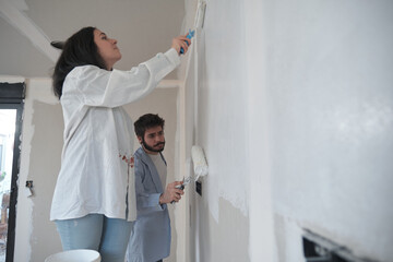 Young couple painting walls in their new house in construction.