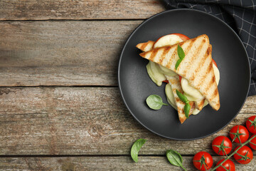 Delicious grilled sandwiches with mozzarella, tomatoes and basil on wooden table, flat lay. Space...