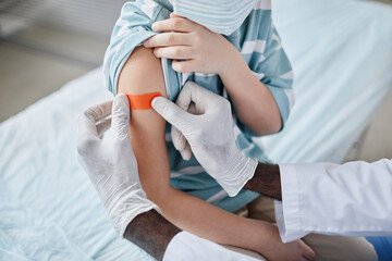Close up of doctor putting patch on shoulder after vaccinating child in clinic, copy space