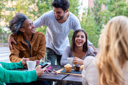 group of friends having fun during breakfast, people of different ethnic groups at the table of a pastry bar, students on break drinking coffee and cappuccino and eating muffins