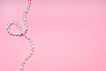 A pearl necklace lies on a pink background