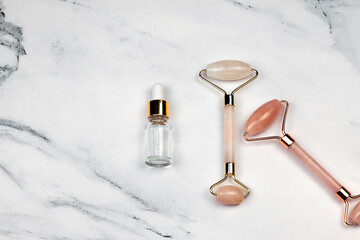 Face Massage pink quartz rollers and face serum oil on white marble background. Skin care facial massage and relaxation. Anti-aging and lifting minimal concept at home.