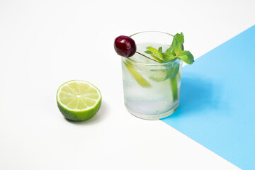 Refreshing detox drink. Water with lime slices, cherry and mint leaves. Summer cocktail on abstract white and blue background.