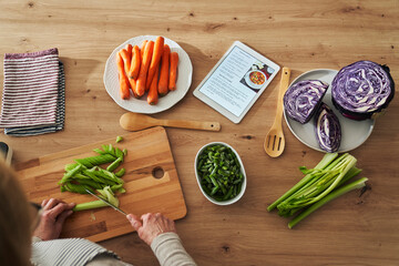 Top view of unrecognizable caucasian senior woman cutting celery while cooking in domestic kitchen