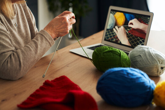 Close up of caucasian senior woman at home learning how to knit from video tutorial