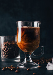close-up on coffee with milk in a transparent glass against the background of coffee beans on a black background