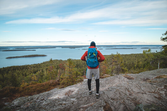 hiker wearing a jacket and carrying a backpack, standing on a rock watching Lake Jatkonjarvi at sunset in Koli National Park, eastern Finland. A man aged 24 wearing sports clothes. Active lifestyle