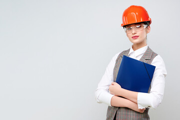 Young female caucasian engineer wearing orange constraction helmet and googles holds blueprint on isolate background