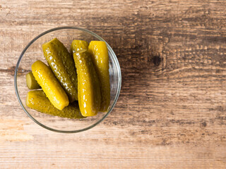 Pickled cucumbers in a bowl on a wooden rustic table and a jar of pickles