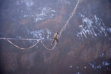 An athlete climbing to a highline to gain a foothold high over a beautiful lake