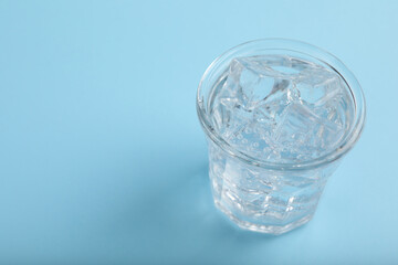 Glass of soda water with ice on light blue background. Space for text