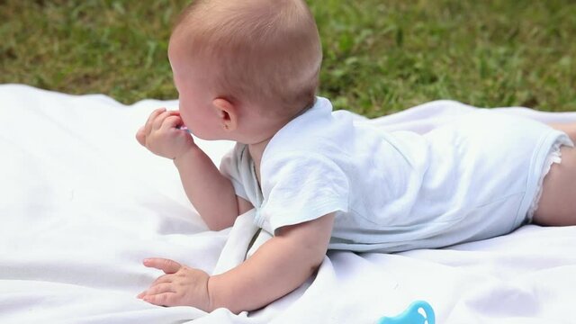 Little newborn girl lying on tummy chewing rattle on blanket, summer day outdoor. Infant having fun outdoors. Infant baby child resting playing learning to crawl. Motherhood teething, babyhood concept