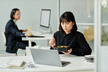 Portrait of young Asian woman enjoying hot lunch at desk in office, copy space