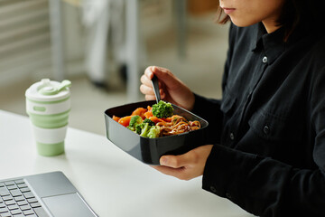 Close up of young woman enjoying healthy lunch with vegetables at break in office, copy space