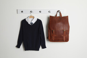 Shirt, jumper and bag hanging on white wall. School uniform