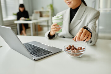 Close up of young businesswoman picking sweet snacks while working at desk in office, copy space - Powered by Adobe